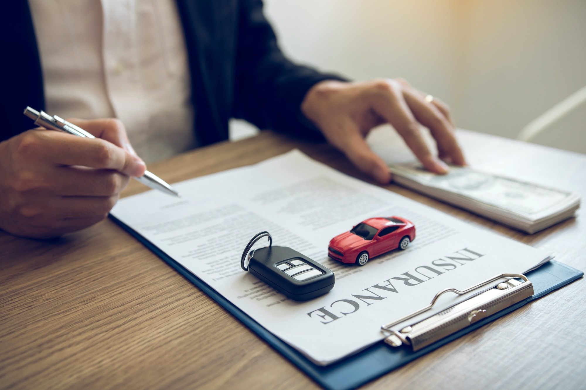 Agent is signing the insurance contract for the car at the document on the desk.